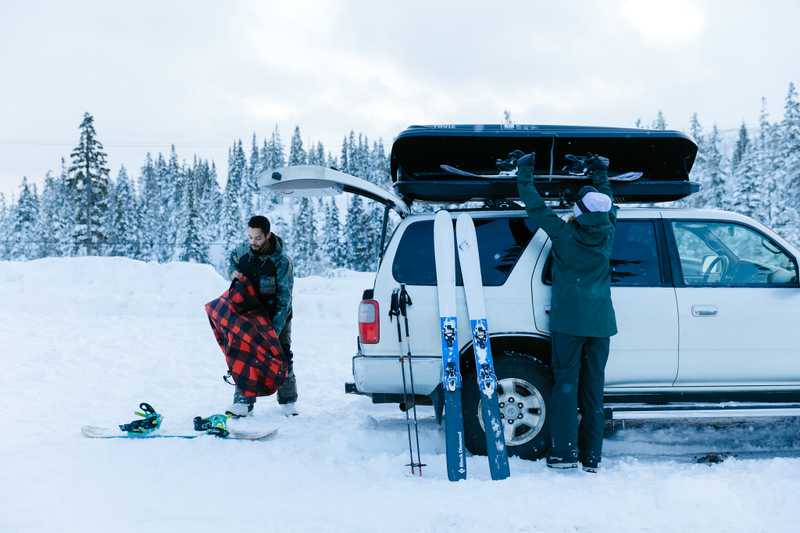 Two people loadings skis and snowboards into a roof rack of an SUV
